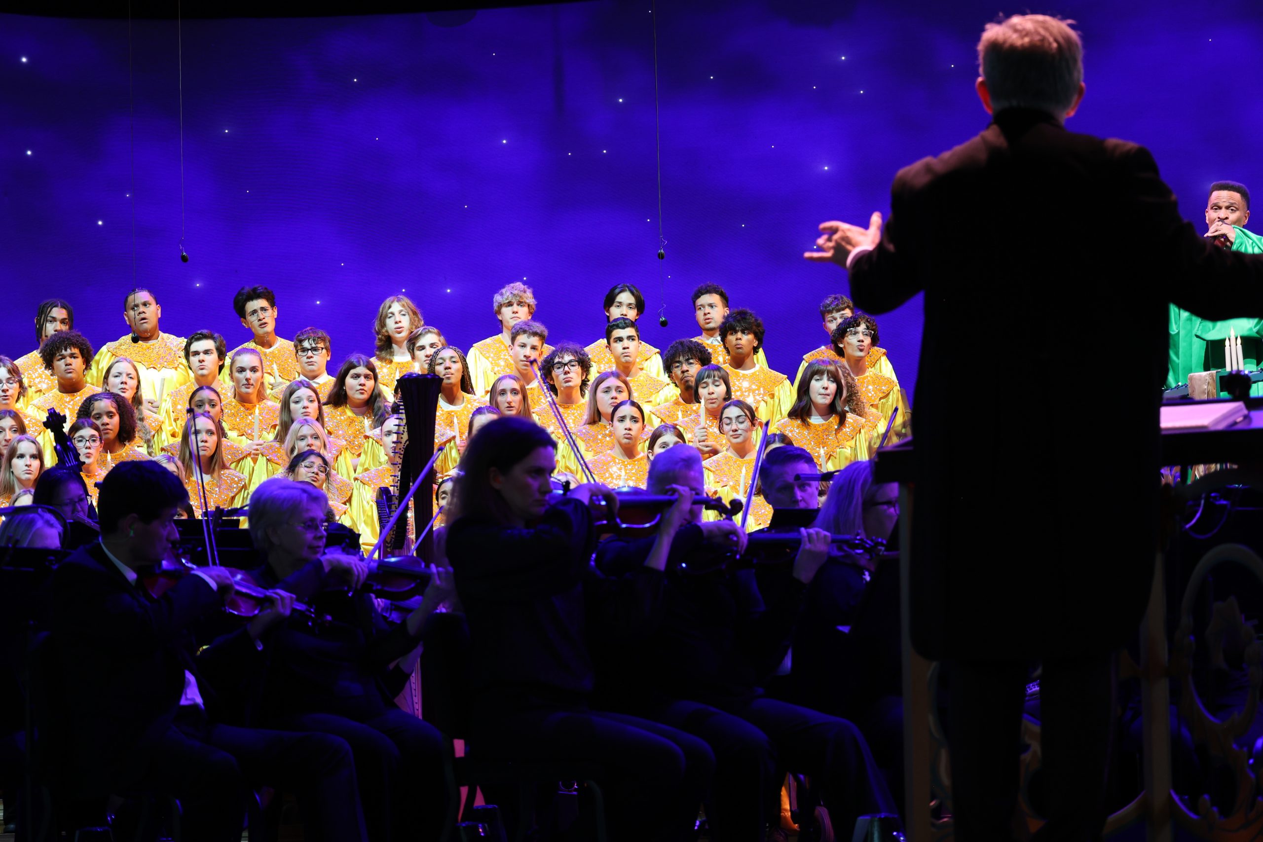 Students performing on stage with orchestra and conductor