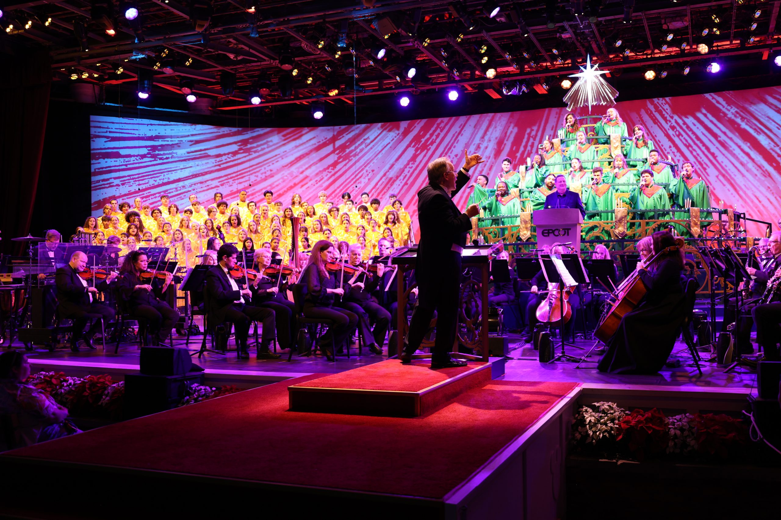 conductor directing an orchestra and choir on stage at the Disney Candlelight Processional