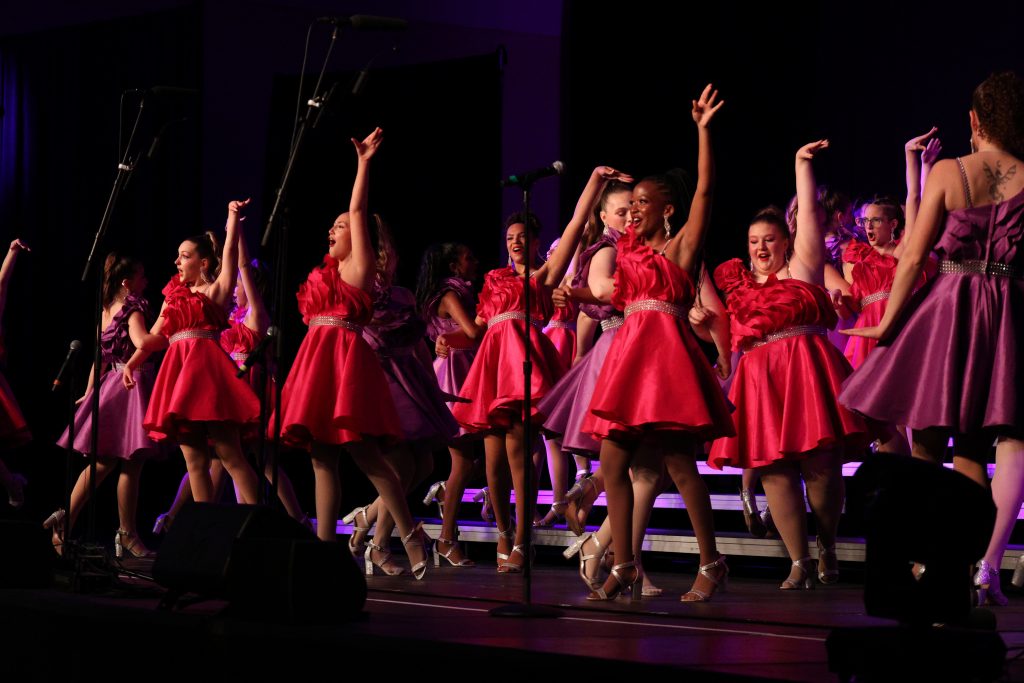 Olentangy High School She-Notes performing on stage in vibrant dresses