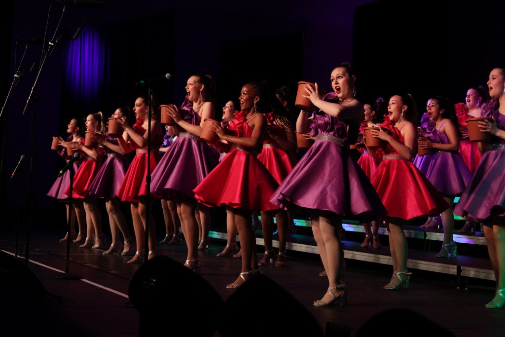 Olentangy High School She-Notes performing on stage in vibrant dresses